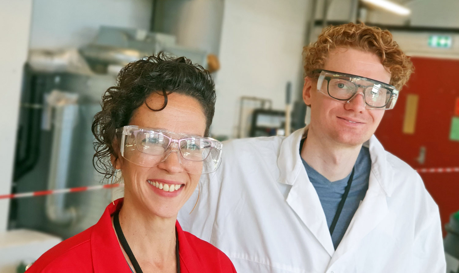 portrait of two researchers, woman in red lab coat and man wearing white lab coat