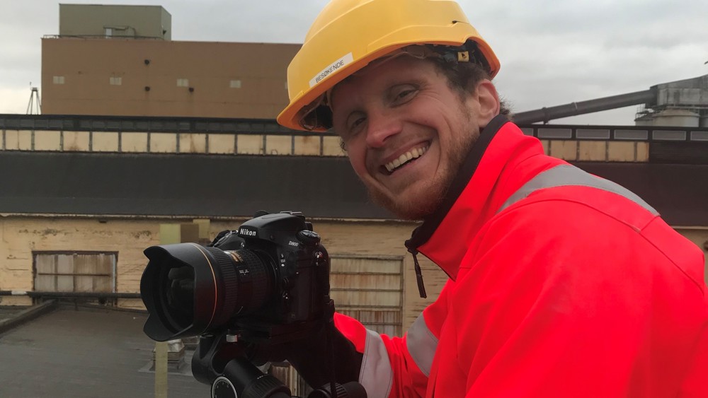 ung mann, gul hjelm, rød arbeidsjakke, kamera, fotojobb, gammelt produksjonsanlegg
