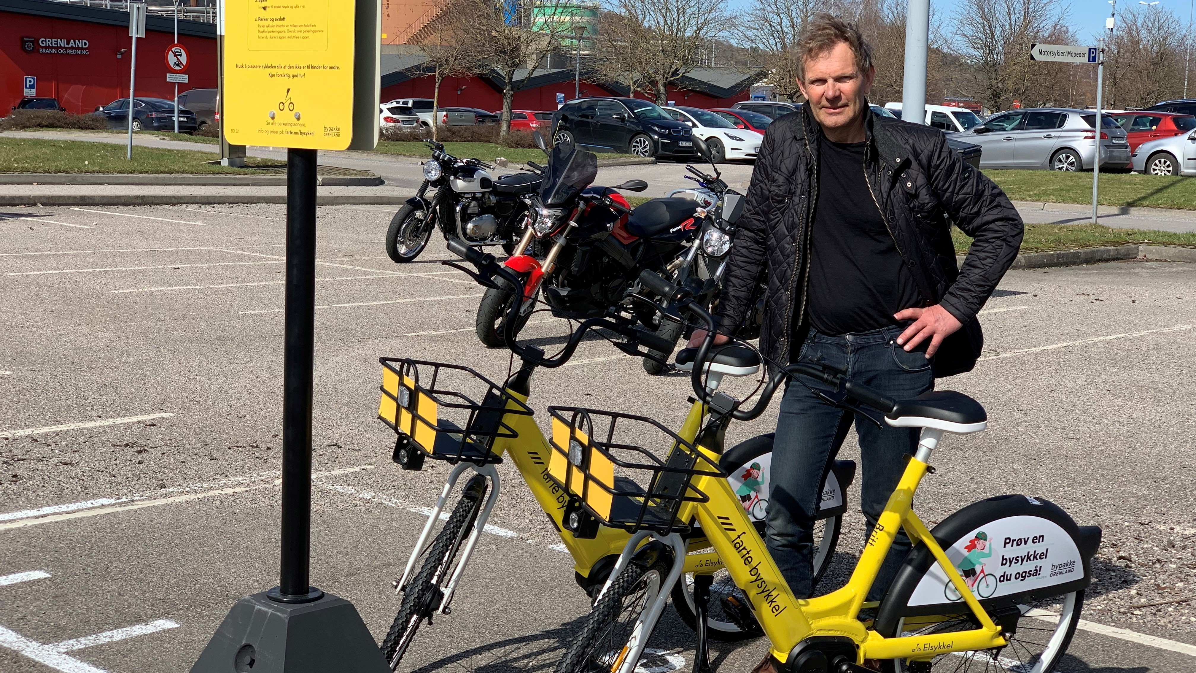 mann poserer ved siden av to gule sykler på en parkeringsplass