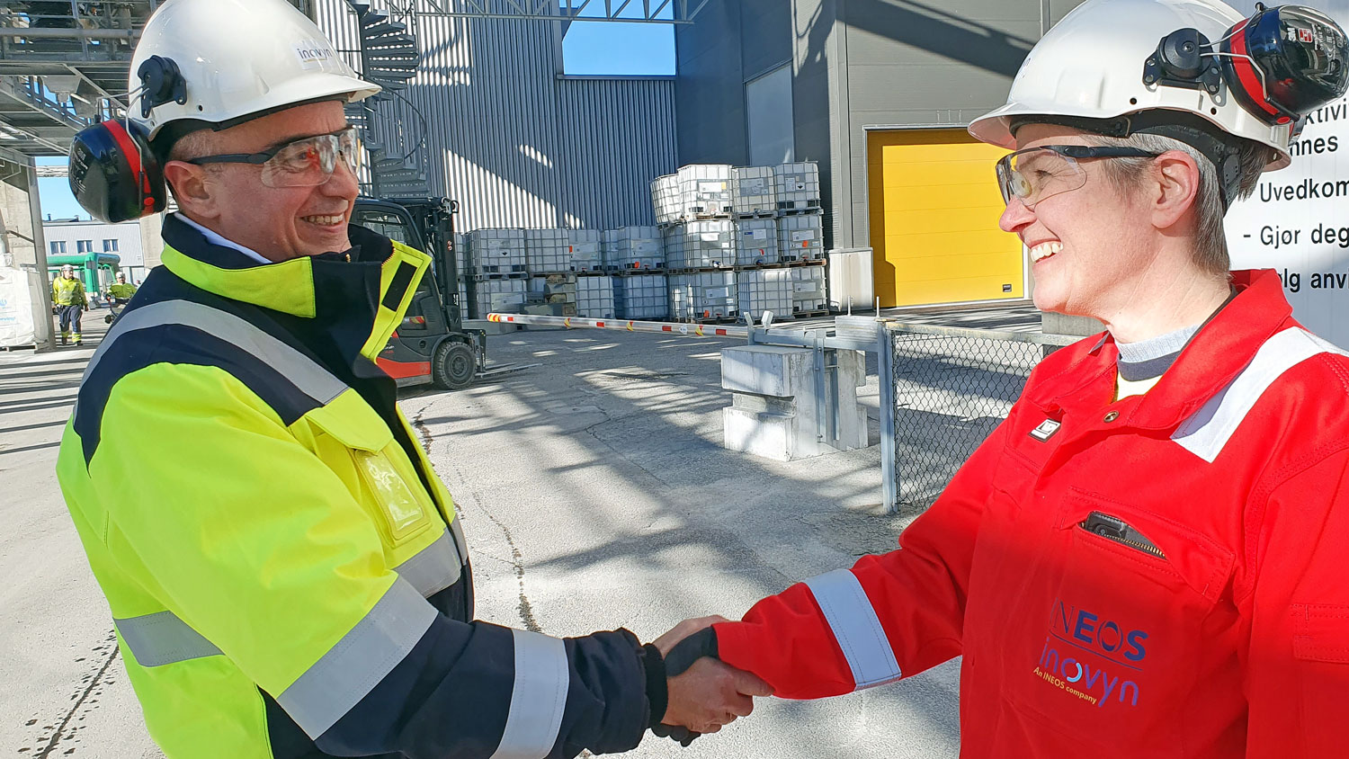 to personer, arbeidsantrekk, hvit hjelm, håndtrykk, fabrikkareal, ute