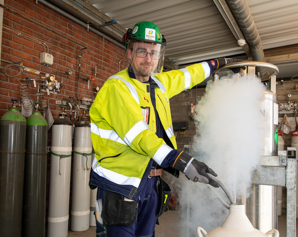 mann i fullt verneutstyr håndterer gasser på et utendørs areal under tak