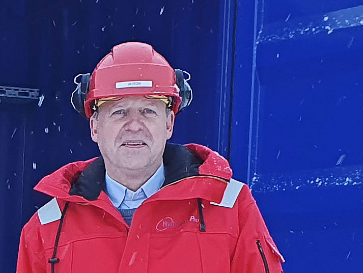 mann i rød hjelm og rød jakke foran blå containerdør