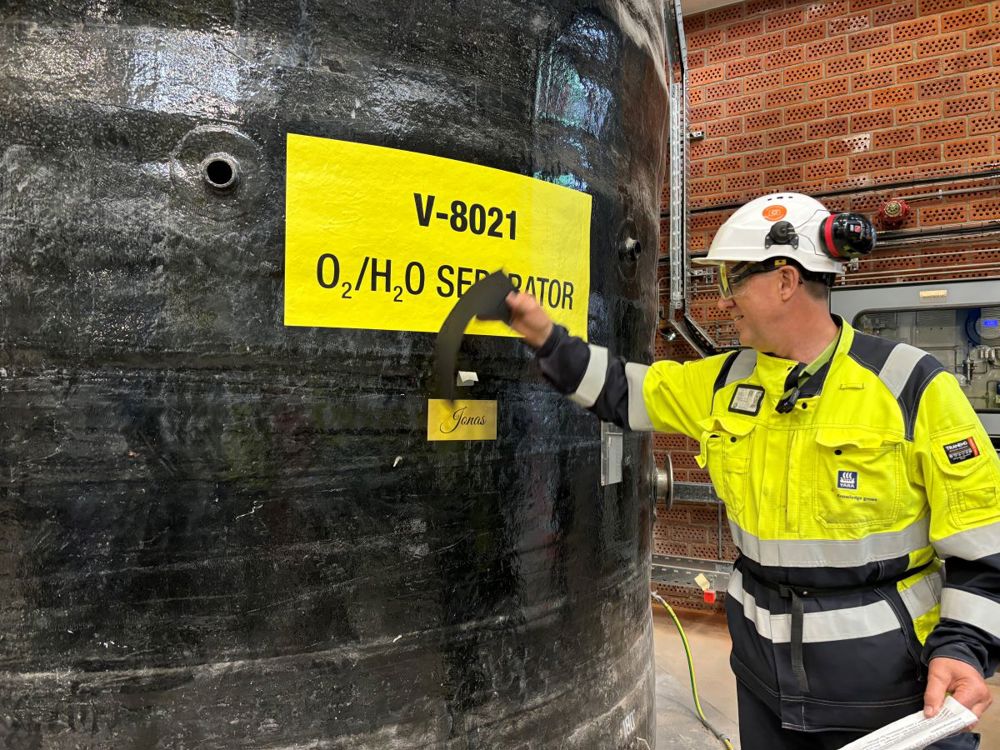 mann river av papir fra tank, og viser fram gullplakett med navnet Jonas på.