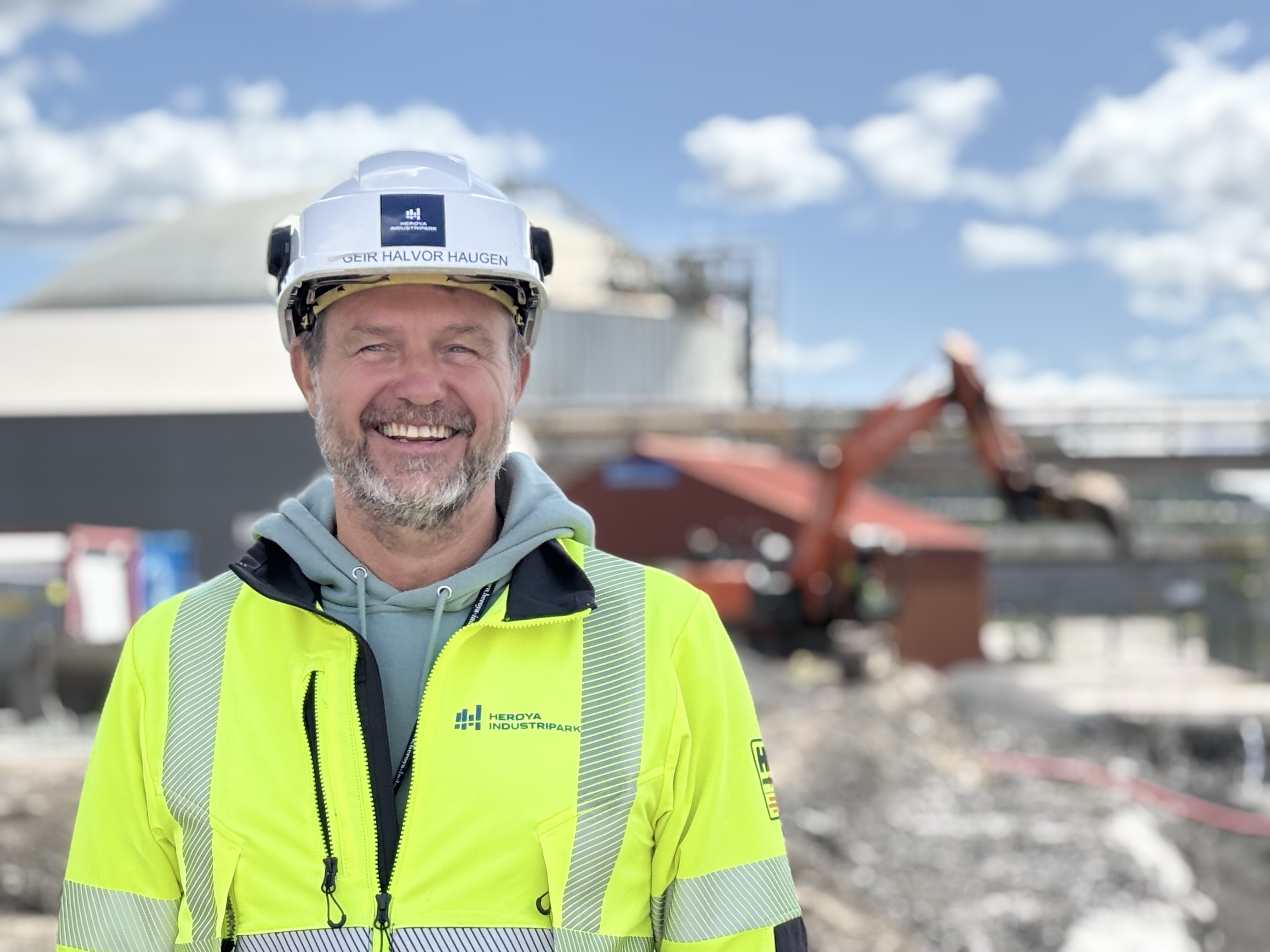 man wearing yellow jacket and white helmet, posing, standing in a construction area, industrial park