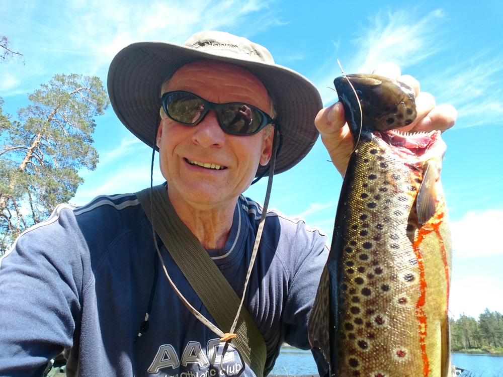 mann med solbriller og hatt og en stor fisk i hånden