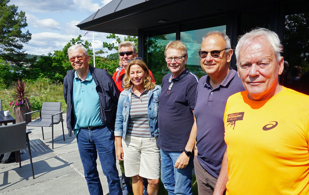 six people posing, standing in line outside a cabin, in the sun,