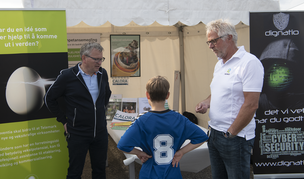 to menn utenfor messetelt snakker med ung gutt med nr 8 på ryggen