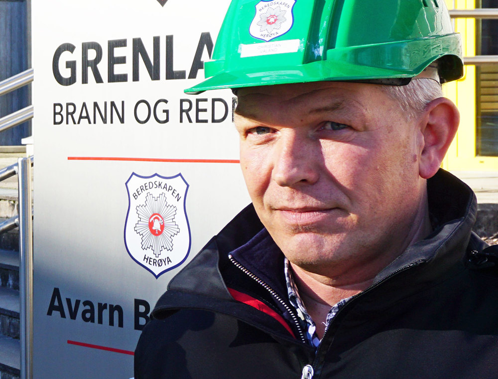 portrett av mann i grønn hjelm, stort skilt med firmalogo i bakgrunnen