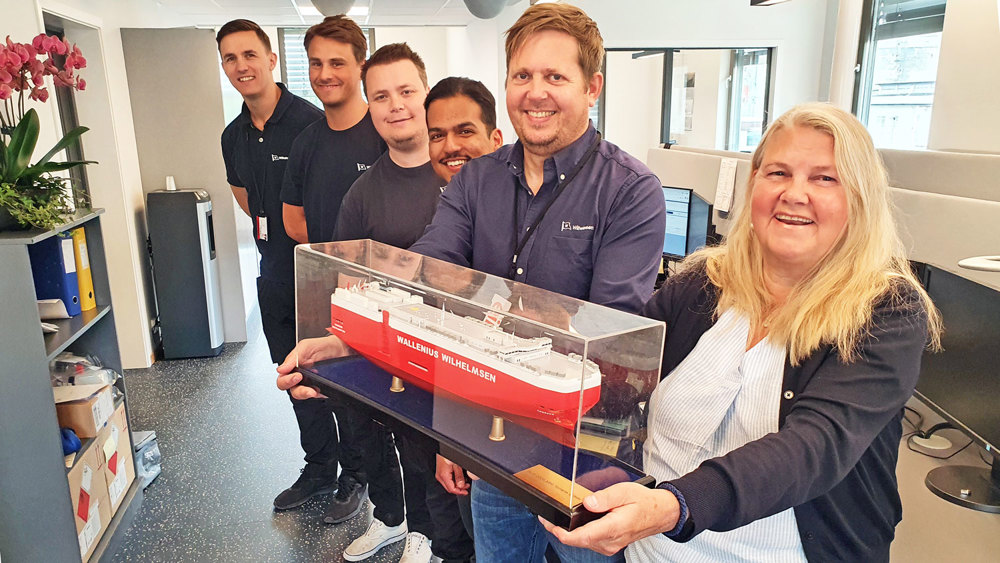 seks ansatte står på rad og holder skipsmodell foran seg