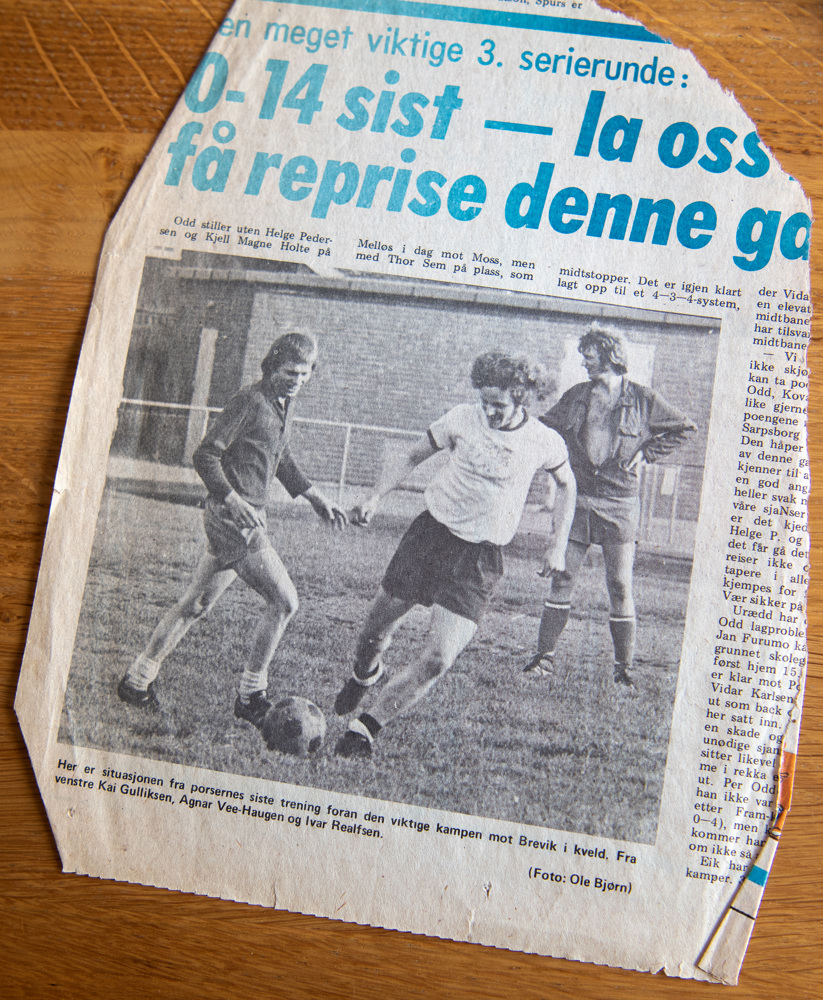 et gammelt avisutklipp med bilde av tre fotballspillere som sparker ball ligger på et bord