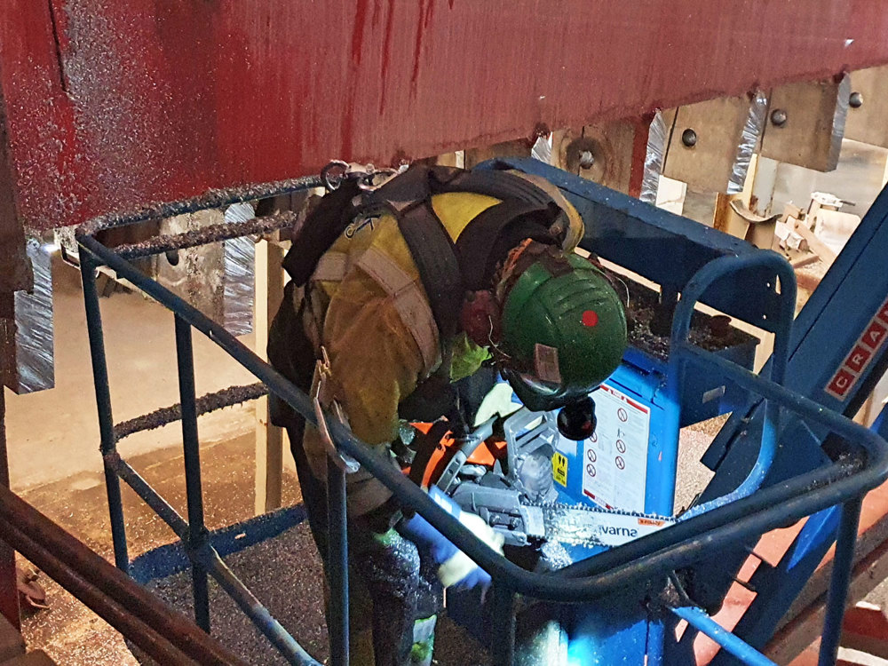 person in a lift basket bending over a chain saw