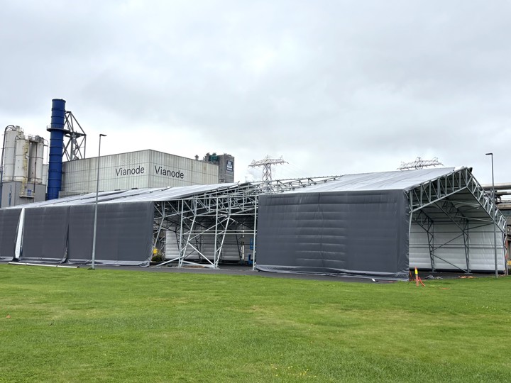 big plastic tent, industry, almost finished, green grass in front, industry buildings background.