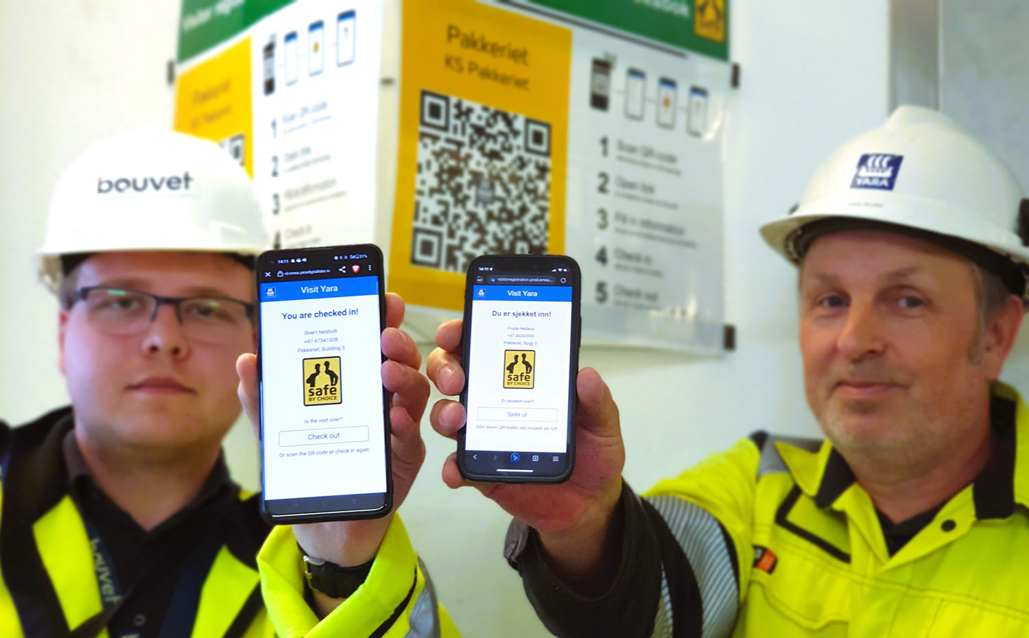 to menn holder frem sine mobiler og viser besøksapp. De har på seg gule jakker og hvite hjelmer, kontormiljø, bruksanvisning for app henger på veggen bak.