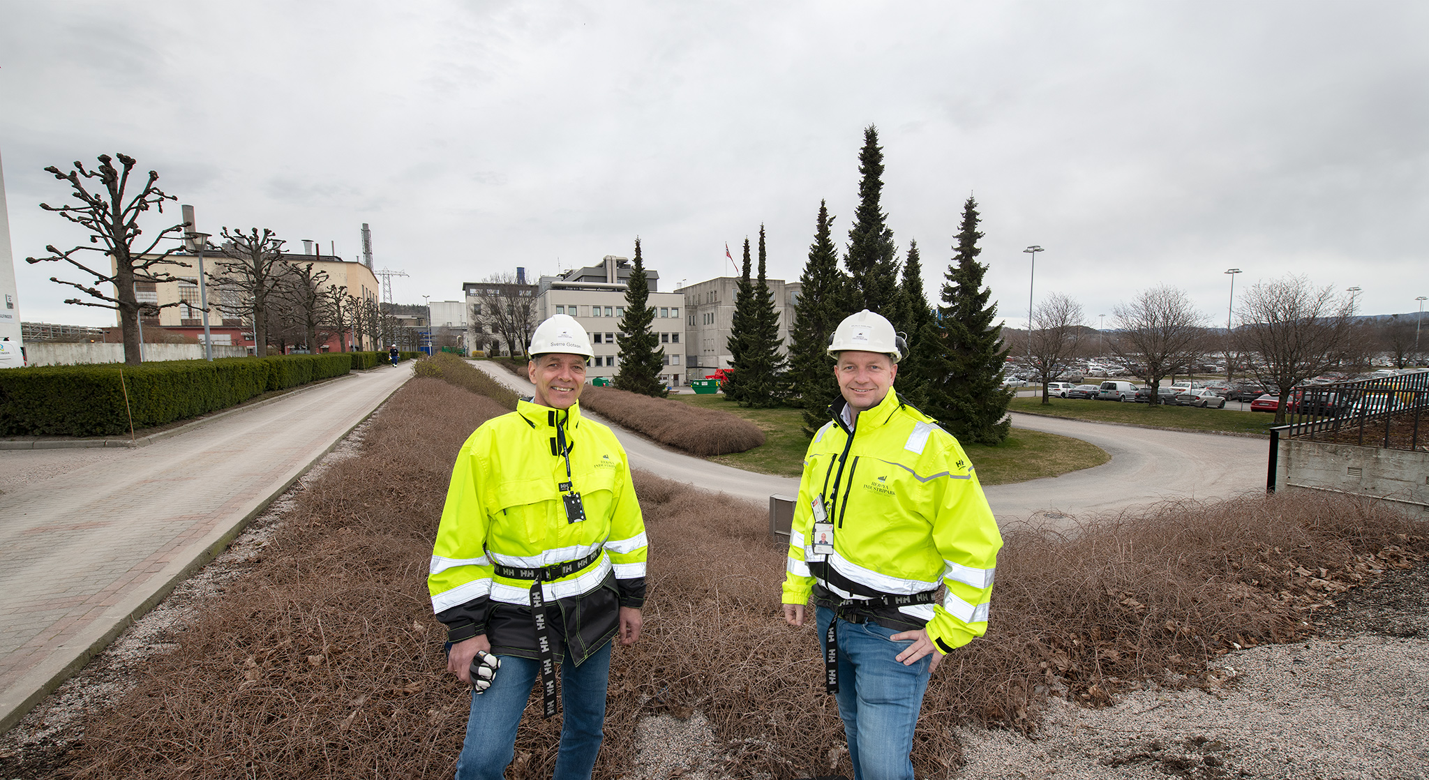 two men standing outside in an industrial park with vacant plot behind them