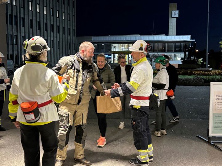 personer iført hvite t-skjorter over arbeidsantrekk møter folk som er på vei til jobb, fabrikkområdet, inngangsport